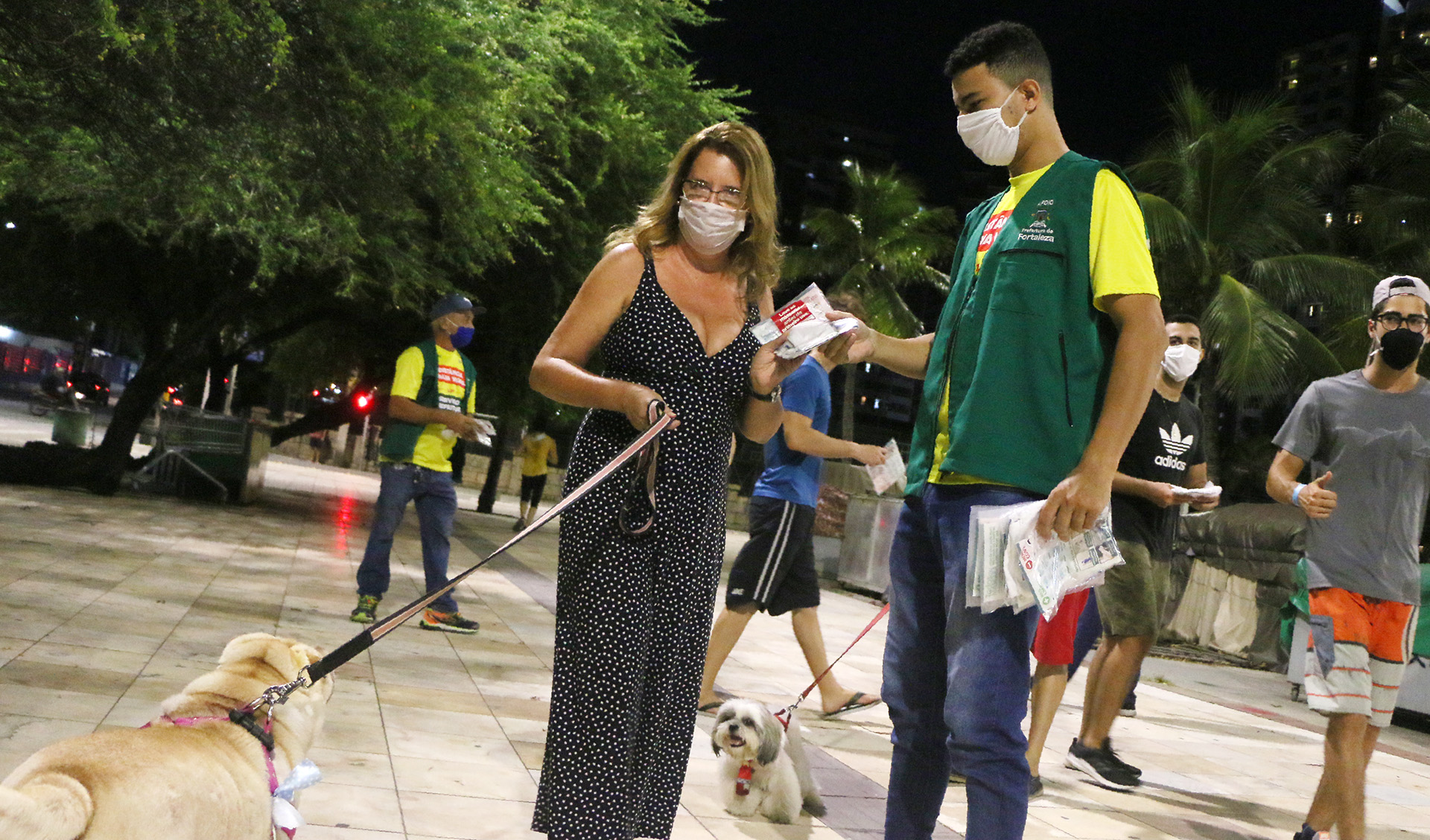 fiscal de máscara entregando kit de máscara para senhora usando máscara e passeando com cachorro em coleira